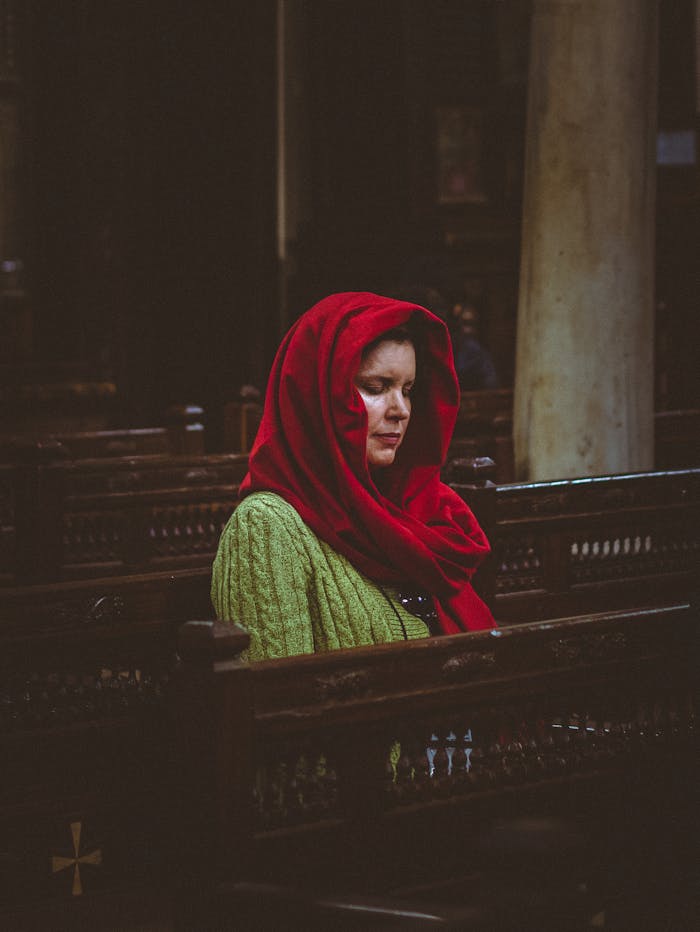 Woman in red headscarf peacefully praying inside an ancient Cairo church.